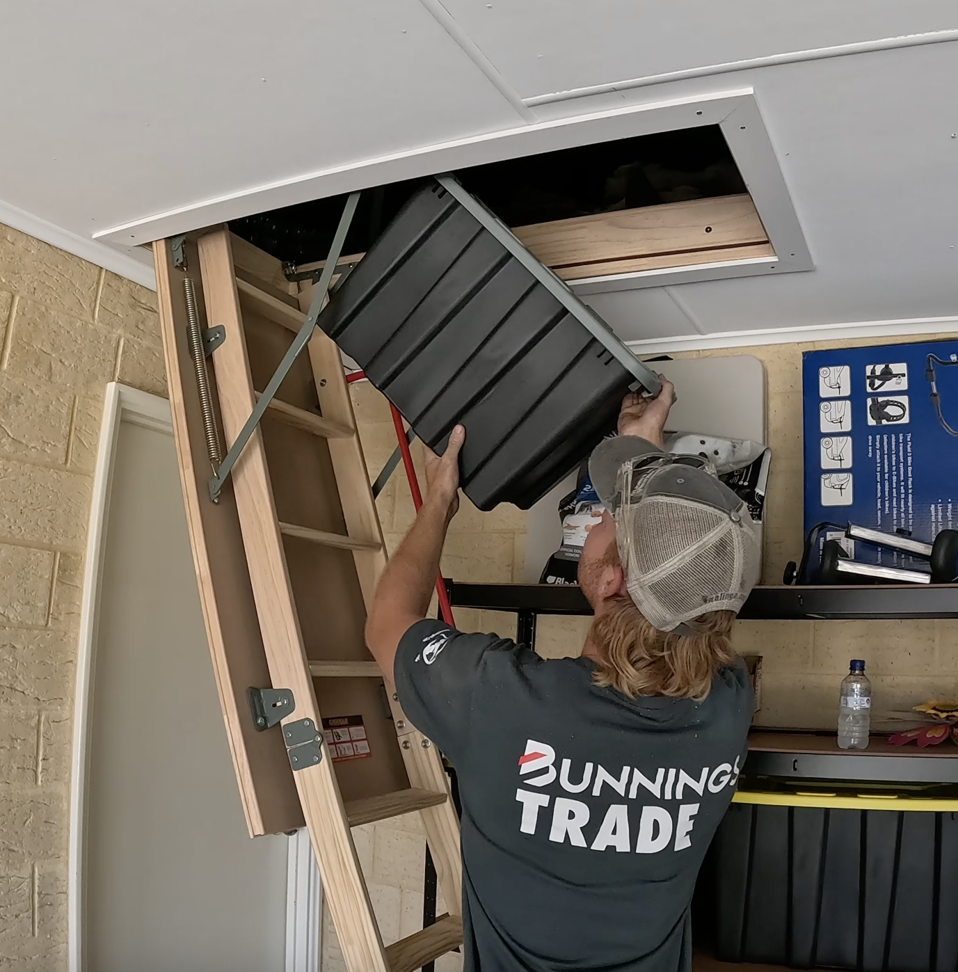 Total Attics installer lifting a storage tub into an attic through a timber ladder hatch